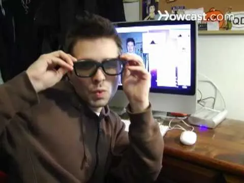Young man wearing glasses poses in front of a computer screen.