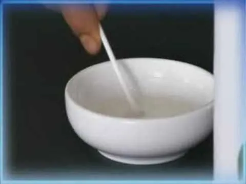 A hand stirring a small bowl with a cotton swab.