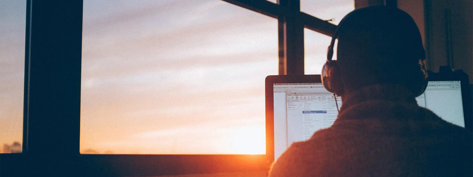 Person working on a computer with headphones at sunset.