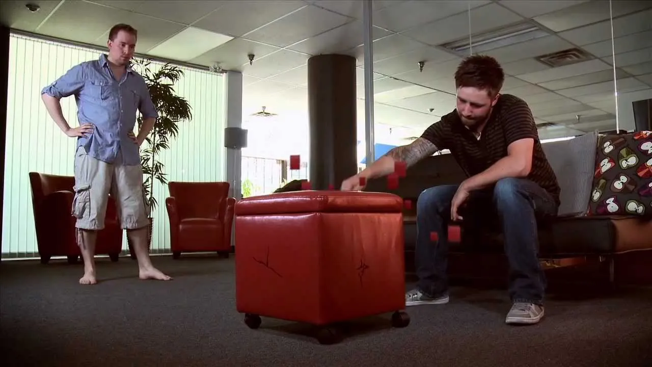 Two individuals in a modern office setting interacting with a leather ottoman.