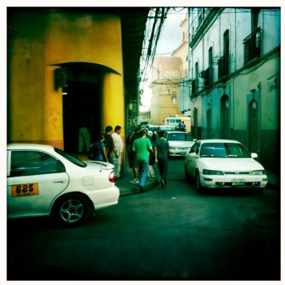 People walking in a narrow street with parked white cars.