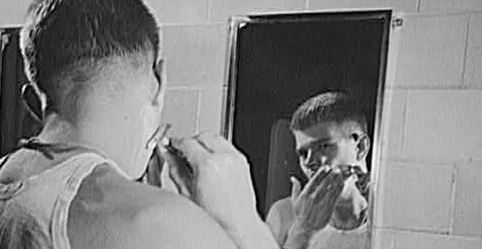 A person shaving in front of a bathroom mirror.