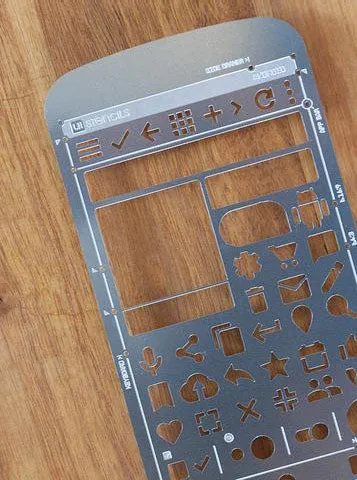 Stainless steel stencil with various shapes cut out on a wooden surface.