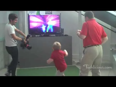Child dancing in front of a television with colorful visuals, accompanied by two adults.