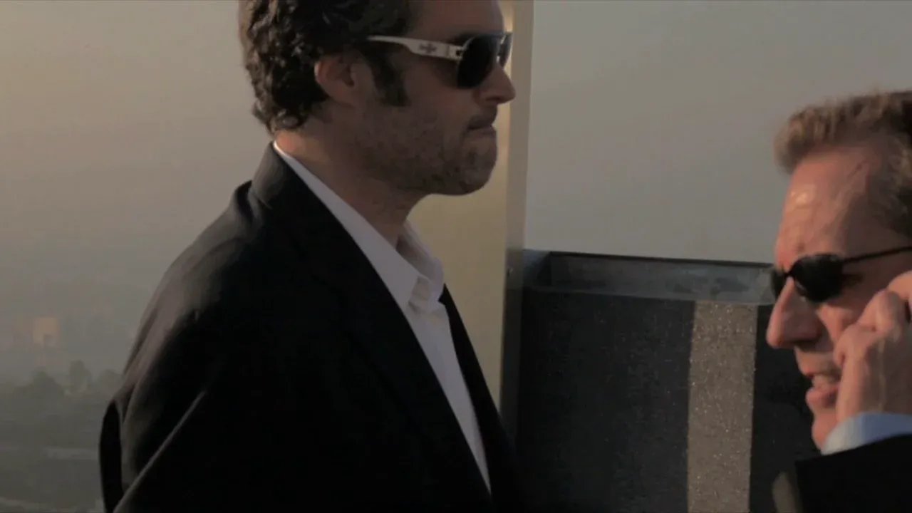 Two men in suits wearing sunglasses, one speaking on the phone.