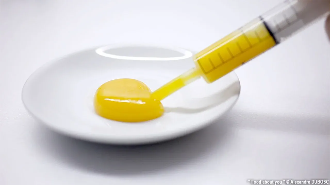 Syringe drawing liquid from an egg yolk on a plate.