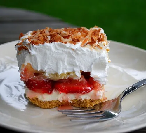Strawberry dessert slice with whipped cream and a crumbly topping on a plate.