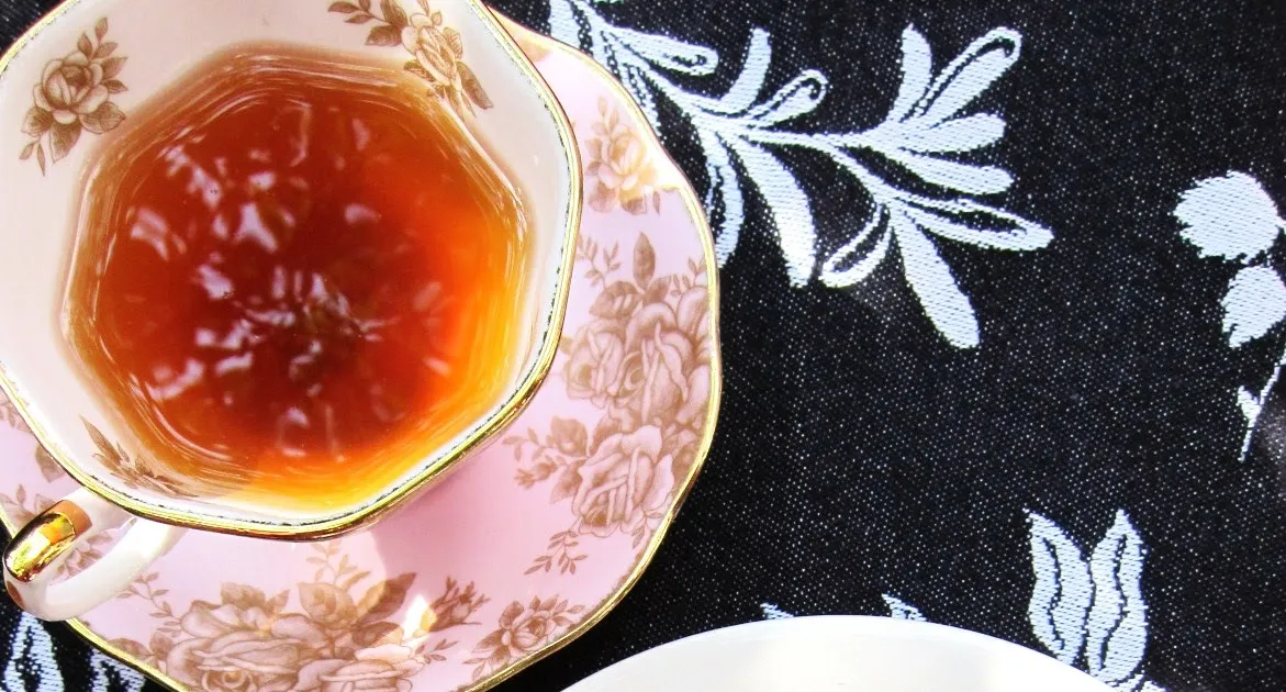A delicate tea cup with tea on a floral patterned tablecloth.