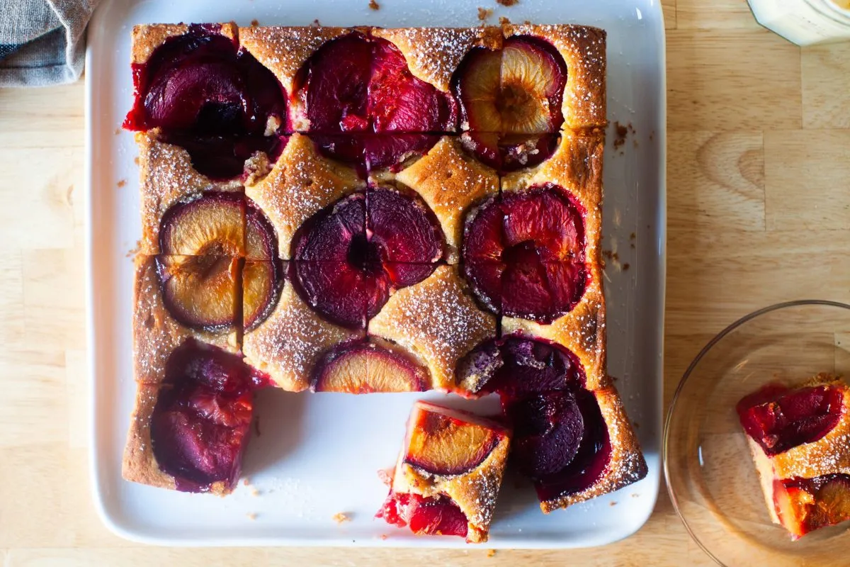Plum cake on a white plate with slices cut out.