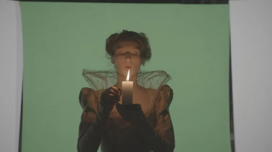Woman in a black dress holding a candle against a green background.