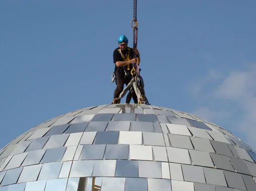 Worker on a dome structure installing roofing materials.