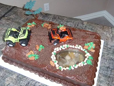 Chocolate birthday cake decorated with toy construction vehicles and a small pond.