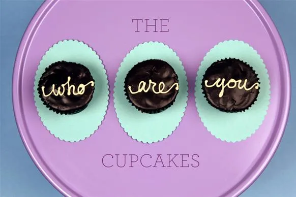 Cupcakes with decorative lettering reading "who are you" on a purple tray.
