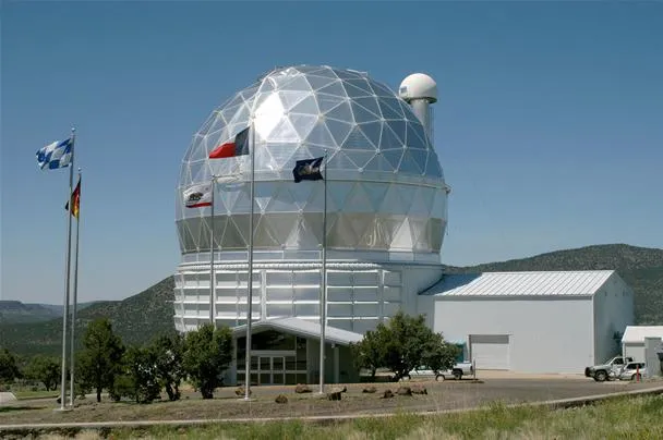 Weather observation dome with flags, surrounded by greenery.