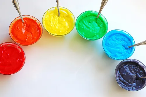 Bowls of vibrant colored frosting arranged in a rainbow pattern.