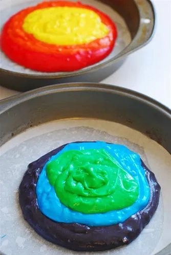 Colorful layers of cake batter in round baking pans.