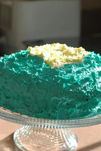Blue frosted cake with yellow topping on a decorative stand.