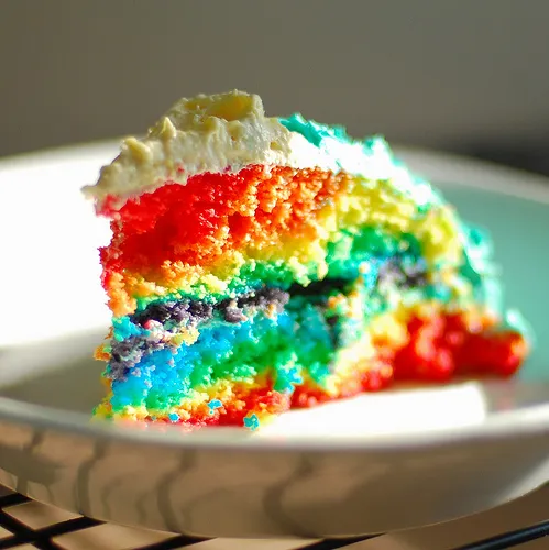 Slice of colorful rainbow cake on a white plate.