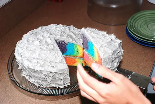 Colorful layered rainbow cake with icing, partially sliced.