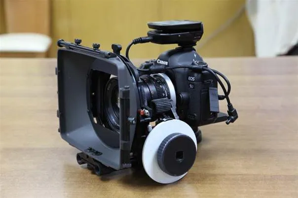 Professional video camera with a lens and matte box on a wooden table.