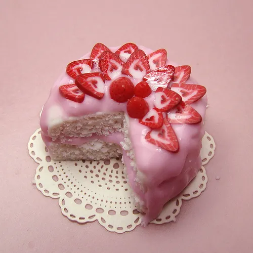 Strawberry cake with pink icing and decorative fruit on a lace doily.