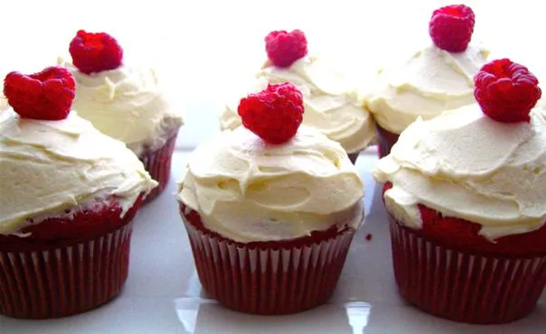 Delicious red velvet cupcakes with cream cheese frosting and raspberries on top.