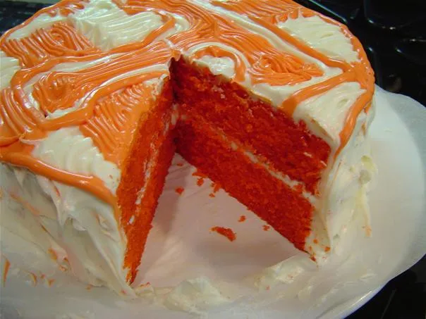 Red velvet cake with orange frosting and a slice removed.