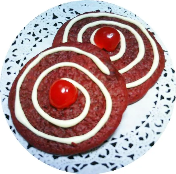 Red velvet cookies with white frosting and a cherry on top, served on a decorative plate.