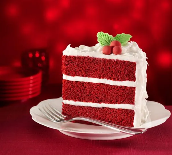 Red velvet cake slice with white frosting and decorative mint leaves.