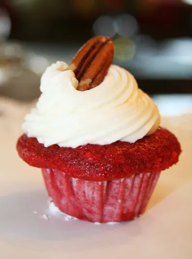 Red velvet cupcake topped with cream cheese frosting and a pecan.