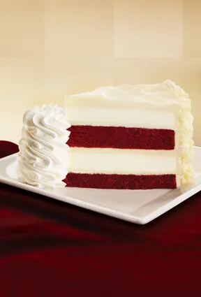 Red velvet cake slice with cream cheese frosting on a plate.