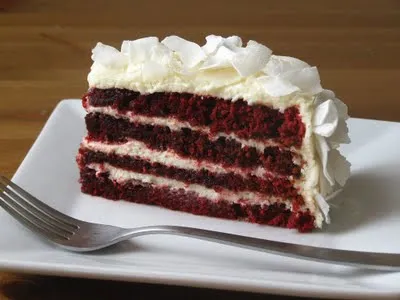 Red velvet cake slice with cream cheese frosting on a plate.