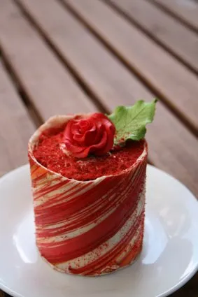Red and white striped cake decorated with a rose and green leaf on a white plate.