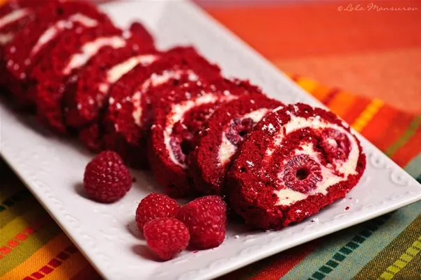 Red velvet cake roll slices on a platter with raspberries.
