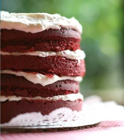 Red velvet cake with cream cheese frosting, layered and presented on a decorative plate.