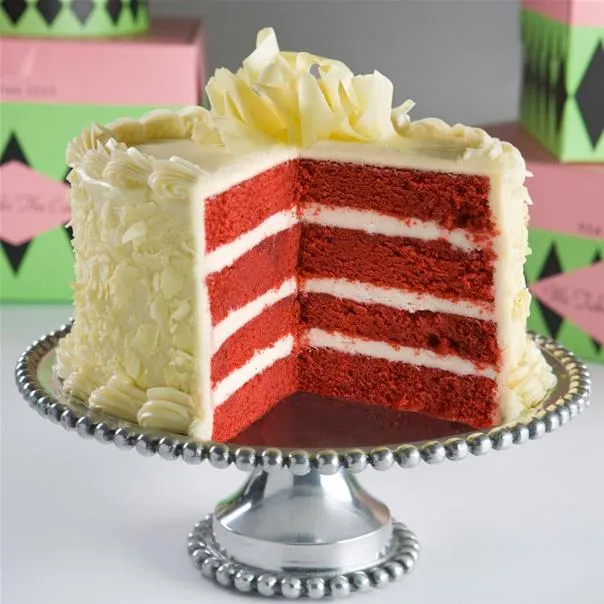 Red velvet cake on a silver cake stand with decorative frosting.