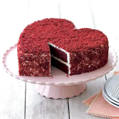 Heart-shaped red velvet cake on a cake stand.