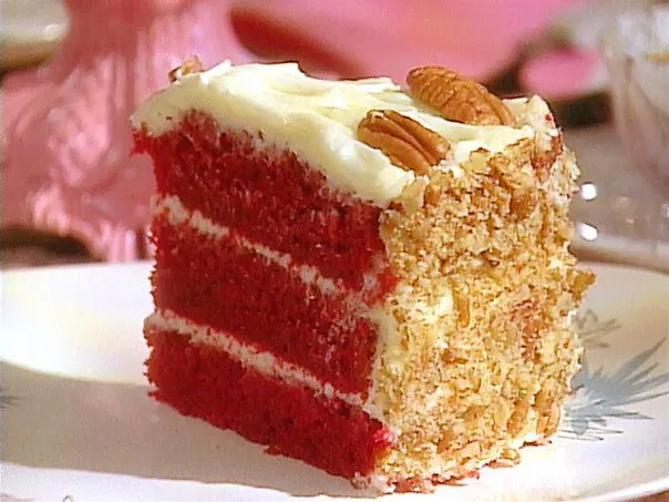 Red velvet cake slice with cream cheese frosting and almond topping on a plate.