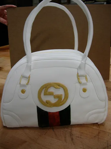 White handbag with a gold logo and striped accents.