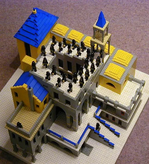 LEGO building model featuring a multi-level structure with blue and yellow rooftops, figures arranged on the rooftop, and an adjacent tower.