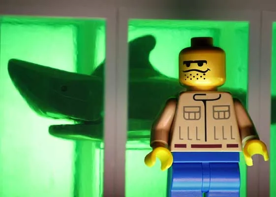Lego figure in front of a green backdrop with a shark silhouette.