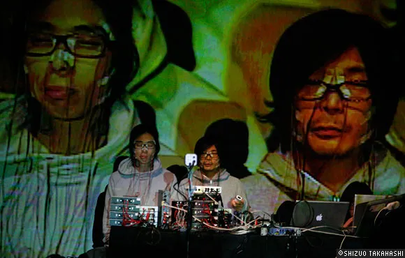Performers at a multimedia art event with projected visuals in the background.