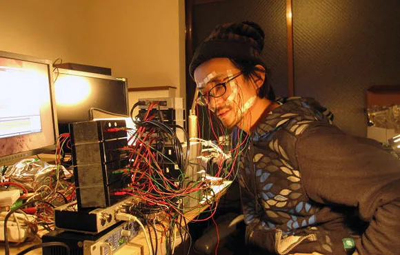 A person working on electronic equipment with numerous wires in a dimly lit room.