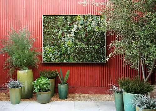 Green vertical garden display on a red wall surrounded by decorative potted plants.