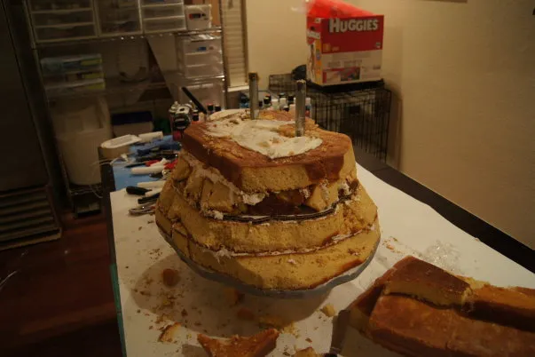 Multi-tiered cake with frosting and decorations in a kitchen setting.