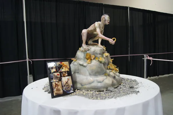 Statue of a figure on a rock, surrounded by small rocks and photographs, displayed on a pedestal.