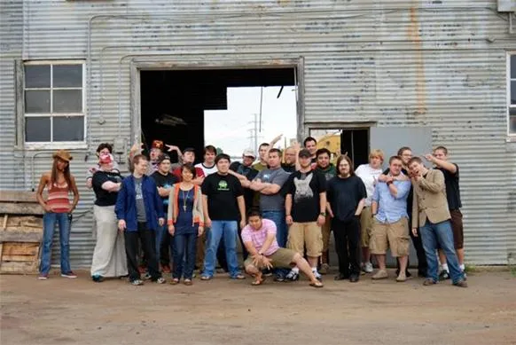 Group photo of people posing together in front of a rustic building.