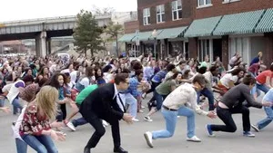 A large group of diverse people participating in a coordinated dance in an urban setting.