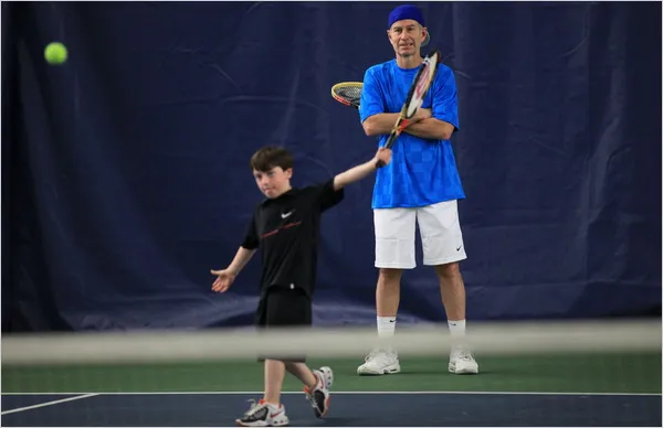 A young boy practicing tennis with a coach.