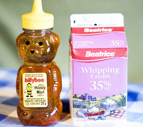 Bottles of honey and whipping cream on a checkered tablecloth.